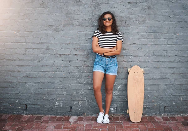 Ich bin sicher ein Skatergirl. Porträt einer jungen Frau, die mit einem Skateboard vor einer grauen Wand steht. — Stockfoto