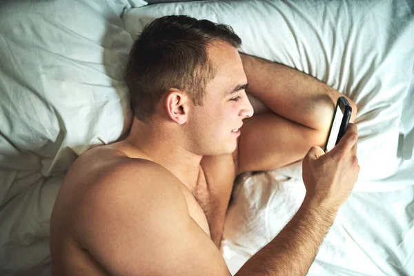 Ser íntimo online. Tiro cortado de um jovem bonito homem sem camisa usando um celular na cama em casa. — Fotografia de Stock