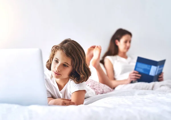 Ingoiati nei loro mondi. Colpo ritagliato di una giovane ragazza che utilizza un computer portatile mentre sua madre legge un libro sullo sfondo. — Foto Stock