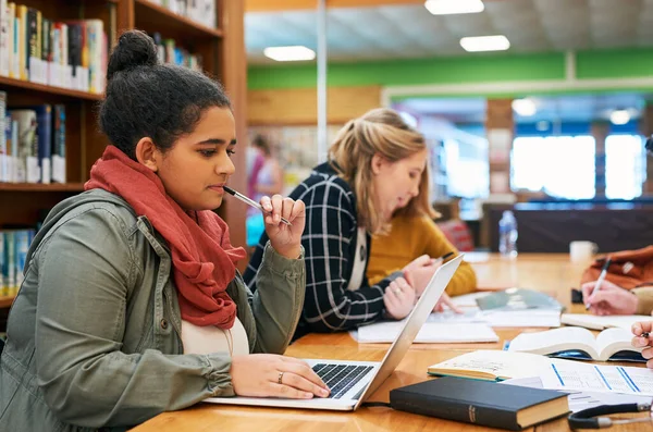 Ella se lo da todo cuando se trata de estudiar. Fotografía de una joven estudiante enfocada trabajando en su computadora portátil y estudiando dentro de una biblioteca. —  Fotos de Stock