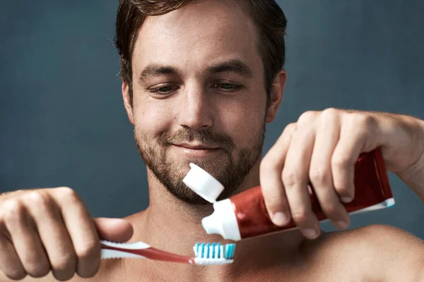 My toothpaste does what yours cant. Cropped shot of a handsome young man brushing his teeth against a grey background. — Stock Photo, Image