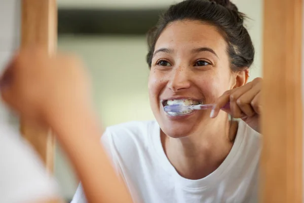 If you want healthy teeth, you have to brush twice a day. Shot of a young woman brushing her teeth while looking into the bathroom mirror.