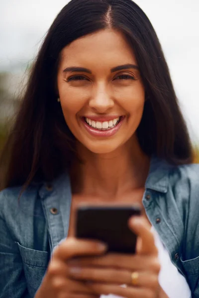 Het is een geweldige dag om te verbinden. Portret van een aantrekkelijke jonge vrouw met een mobiele telefoon in een park. — Stockfoto