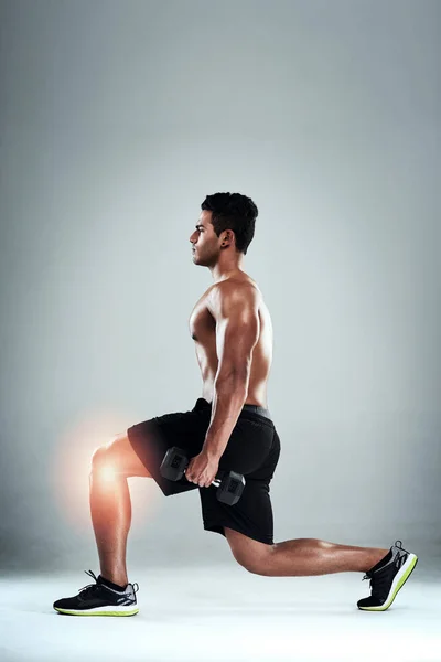 Los brotes pueden poner tensión en las rodillas. Estudio de un joven deportista haciendo ejercicio con una rodilla lesionada sobre un fondo gris. — Foto de Stock