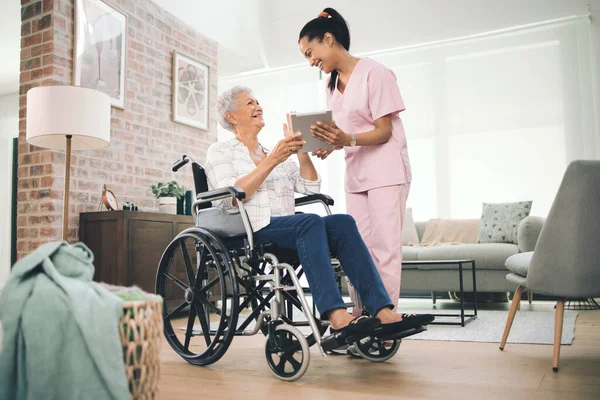Ik heb al je grote momenten vastgelegd. Foto van een jonge verpleegster die informatie deelt vanaf haar digitale tablet met een oudere vrouw in een rolstoel. — Stockfoto