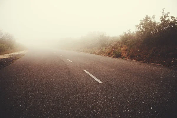Into the mist. Low-angle view of a road fading into fog. — Stock Photo, Image