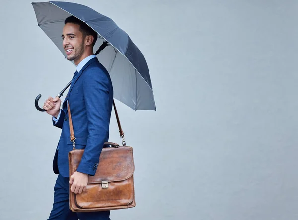 Hes got you covered. Cropped shot of a handsome young businessman posing in studio with his satchel and umbrella against a grey background.