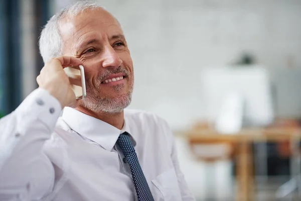 La gente lo llama por consejo de negocios. Fotografía de un hombre de negocios maduro sonriente hablando por celular mientras trabajaba en una oficina. —  Fotos de Stock