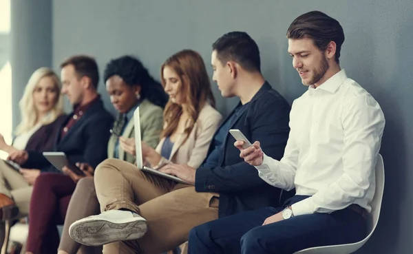 La cola del éxito. Fotografía de un grupo de empresarios que utilizan diferentes dispositivos inalámbricos mientras esperan una entrevista. —  Fotos de Stock