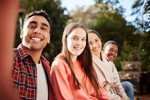 Venner på skolen. Portrett av fire unge studenter som tar selfies mens de sitter utenfor skolen i pausen. – stockfoto