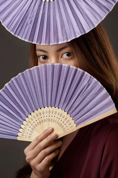 Dont hide your heritage. Cropped portrait of an attractive young woman posing with fans in studio against a grey background.