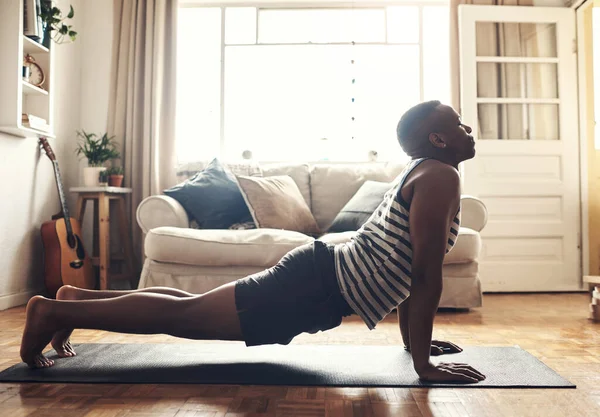 Comienza el día con buenos hábitos. Tiro de un joven deportivo haciendo un estiramiento de cobra mientras hace ejercicio en casa. — Foto de Stock
