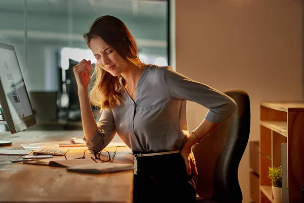 Het effect van uren zitten. Shot van een aantrekkelijke jonge zakenvrouw houdt haar rug in pijn tijdens het werken laat in het kantoor. — Stockfoto