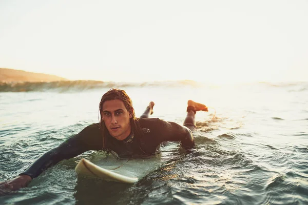 Surfen gaat over het ritme van de oceaan. Portret van een jonge man peddelend op een surfplank in de zee. — Stockfoto