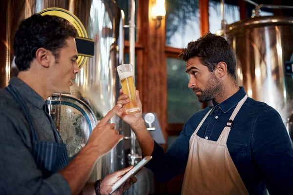 Auch die Farbe des Bieres sagt viel darüber aus. Aufnahme von zwei fokussierten jungen männlichen Geschäftsinhabern, die tagsüber eine frische Charge Bier in ihrer Brauerei testen. — Stockfoto