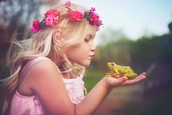 Tu deviendras prince si je t'embrasse. Tourné d'une petite fille joyeuse tenant une grenouille et entrant pour un baiser tout en se tenant dehors dans la nature. — Photo