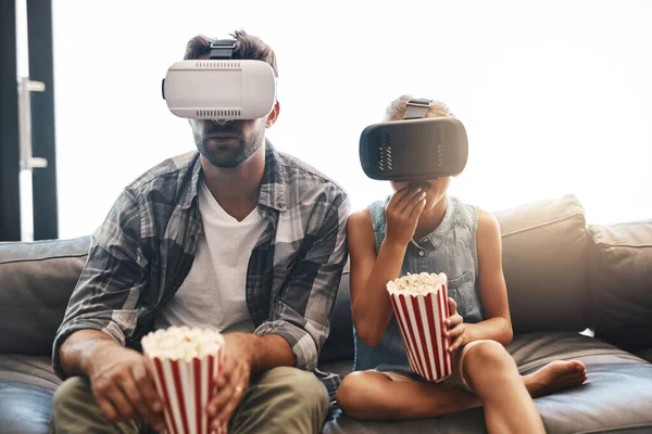 Kul för alla åldrar. Skott av en far och dotter äta popcorn och titta på filmer med virtuell verklighet headset hemma. — Stockfoto