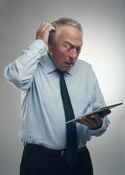 Przegapiłem spotkanie z inwestorami. Zdjęcie starszego biznesmena stojącego samotnie na szarym tle studia i wyglądającego na zdezorientowanego podczas korzystania z tabletu cyfrowego. — Zdjęcie stockowe