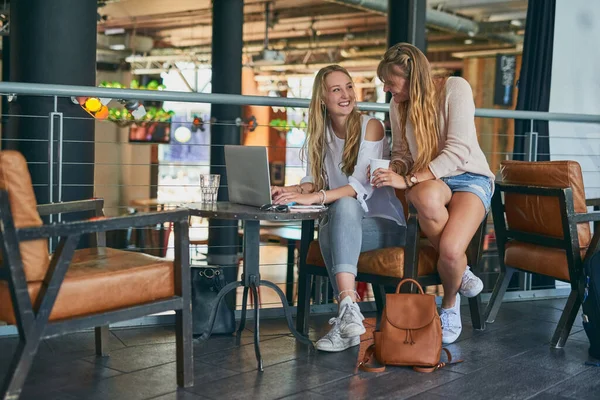 El blog se ve muy bien. Largura completa de un tiro de dos atractivos amigos jóvenes utilizando un ordenador portátil mientras está sentado en un café. —  Fotos de Stock