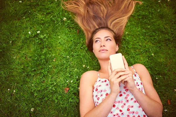Cosa devo rispondere? Girato di una giovane donna che usa il suo cellulare mentre giace sull'erba. — Foto Stock