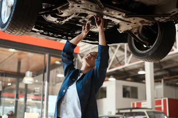 Não há nada como ser capaz de consertar algo com as próprias mãos. Tiro de uma mecânica feminina trabalhando sob um carro levantado. — Fotografia de Stock