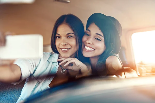 Vergessen Sie nicht, die Erinnerungen zu sammeln. Aufnahme von zwei glücklichen Freunden, die Selfies mit einem Handy auf einem Roadtrip machen. — Stockfoto