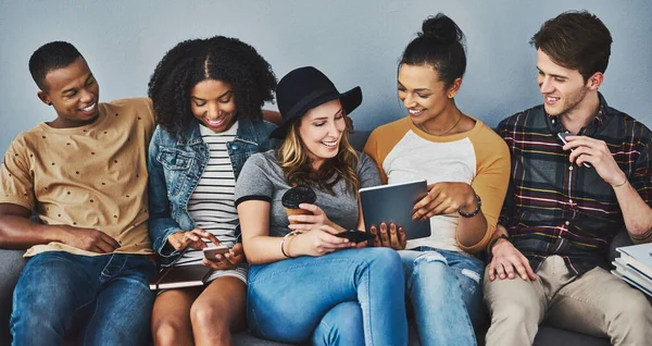 Heeft social media de betekenis van social media veranderd. Studio shot van jongeren zittend op een bank en met behulp van draadloze technologie tegen een grijze achtergrond. — Stockfoto