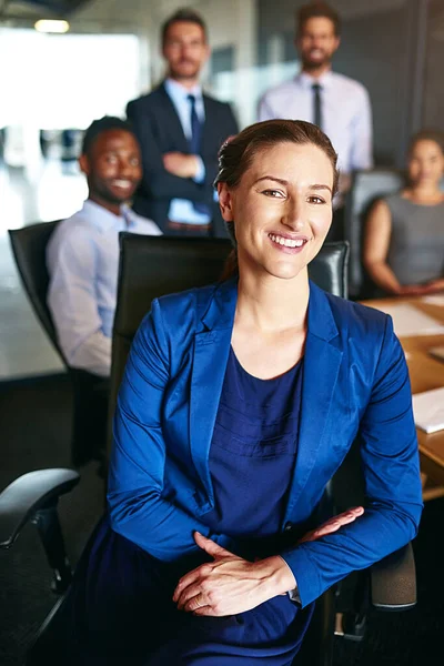C'est une équipe montante de stars. Portrait d'une femme d'affaires souriante assise dans un bureau avec des collègues en arrière-plan. — Photo