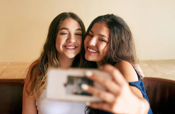 Prendre des selfies avec sa meilleure amie. Plan recadré de deux jolies jeunes femmes prenant des selfies dans leur café local. — Photo