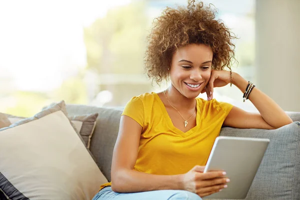 Sua revista online favorita a mantém entretida por horas. Tiro de uma jovem mulher usando um tablet digital em um dia relaxante em casa. — Fotografia de Stock