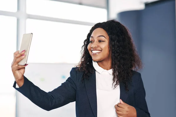 Tijd om het te laten gebeuren, maar eerst een selfie. Foto van een jonge zakenvrouw die een selfie maakt met een smartphone in een modern kantoor. — Stockfoto