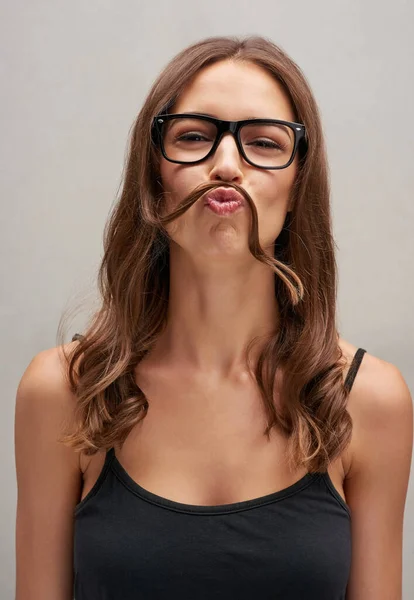 Parece que es Movember otra vez. Retrato de estudio de una joven atractiva posando con el pelo sobre el labio sobre un fondo gris. — Foto de Stock