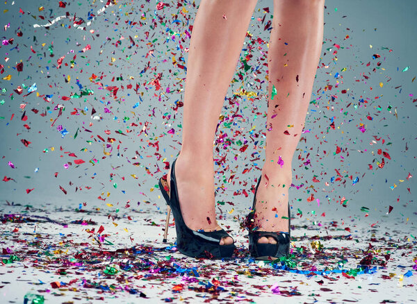 Готов к вечеринке? Студийный снимок молодых женщин на каблуках с конфетти, падающей на сером фоне.