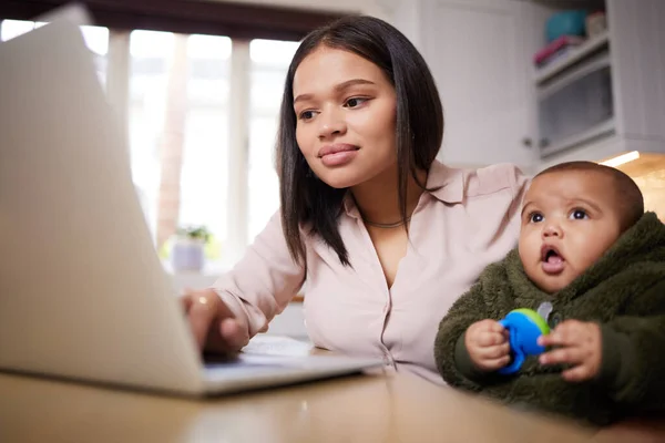 Super woman doing her thing. Shot of a young woman using a laptop while caring for her adorable baby at home. — Stock Photo, Image