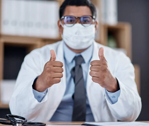 Saudando todos os trabalhadores da linha de frente na luta contra o covid-19. Retrato de um jovem médico usando uma máscara facial e mostrando os polegares para cima em seu escritório. — Fotografia de Stock