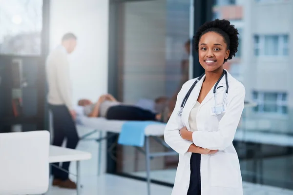 I miei pazienti ricevono sempre le migliori cure. Ritratto ritagliato di una dottoressa in piedi nel suo ufficio con pazienti sullo sfondo. — Foto Stock