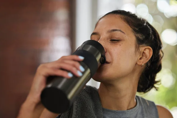 Ik heb het goed gedaan vandaag. Opname van een sportieve jonge vrouw die water drinkt tijdens het sporten in een fitnessruimte. — Stockfoto