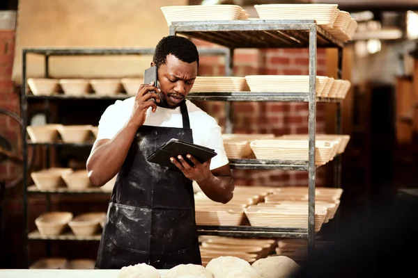 Мені сьогодні знадобиться додаткова допомога з наказом. Обрізаний знімок чоловічого пекаря, який розмовляє по телефону, використовуючи цифровий планшет на роботі . — стокове фото