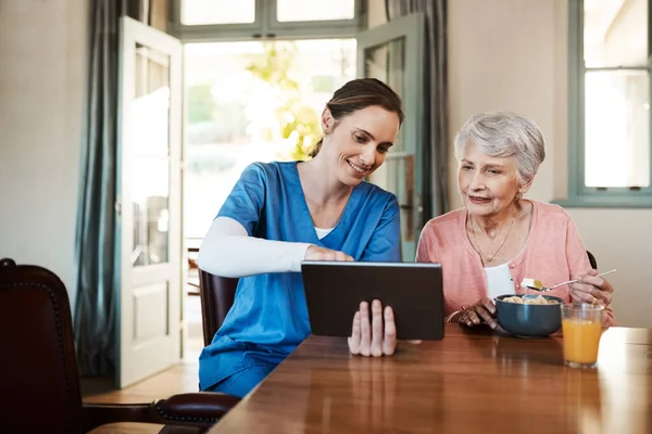 Vea lo fácil que es de usar. Fotografía de una joven enfermera y una mujer mayor usando una tableta digital a la hora del desayuno en un hogar de ancianos. — Foto de Stock