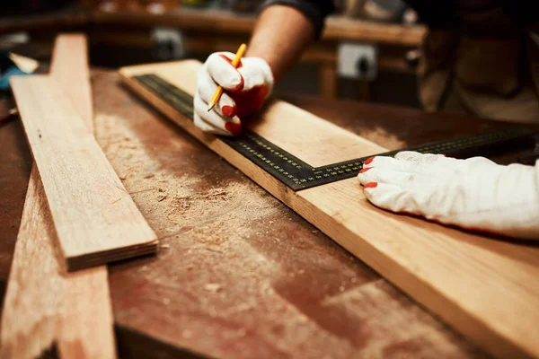 Ce sera plus que ce dont nous avons besoin. Gros plan d'un charpentier masculin méconnaissable faisant des mesures sur un morceau de bois à l'intérieur d'un atelier la nuit. — Photo