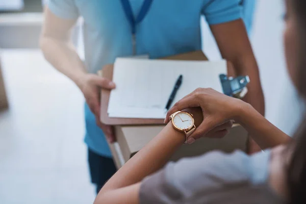 Mi aspettavo questo pacco. Colpo ritagliato di una donna d'affari non identificabile che controlla l'ora sul suo orologio mentre il corriere arriva con una consegna. — Foto Stock