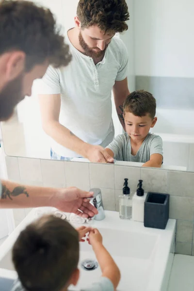 Zbavte se bakterií umýváním rukou. Vystřižené záběr na mladého pohledného otce pomáhá jeho rozkošný malý chlapec umýt si ruce v koupelně doma. — Stock fotografie