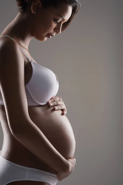 Livet rör sig inom dig, ovärderlig. Studio skott av en vacker ung gravid kvinna poserar i underkläder mot en grå bakgrund. — Stockfoto
