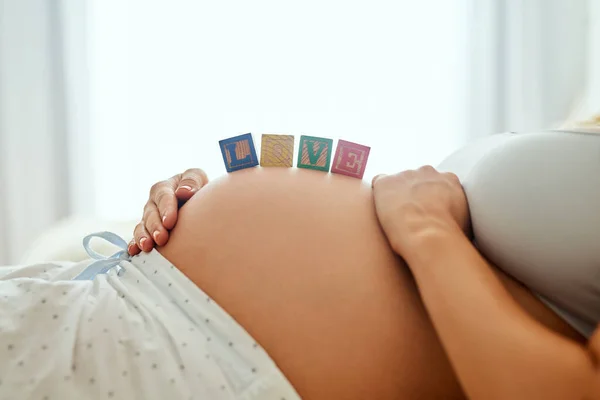 Já tenho tanto amor por ti. close-up tiro de uma mulher grávida deitado com blocos de madeira do bebê em sua barriga. — Fotografia de Stock