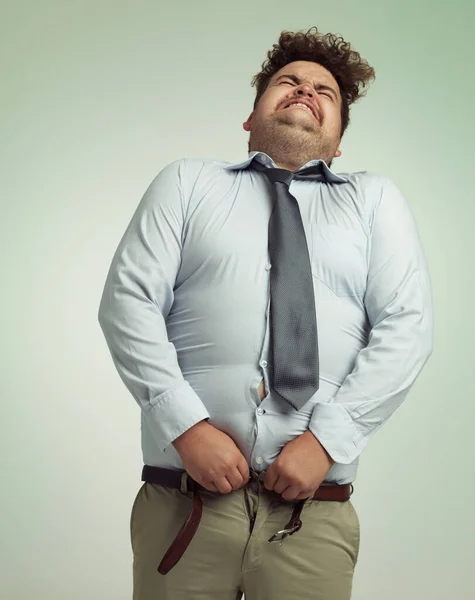 Willing his pants closed. Humorous studio shot of an overweight businessman trying to button his pants. — Stock Photo, Image