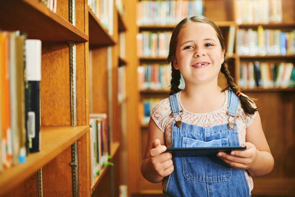 Dit is bijna een boek. Portret van een vrolijk jong meisje op een digitale tablet terwijl ze overdag in een bibliotheek staat. — Stockfoto