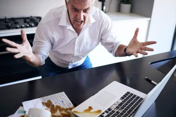 Che diavolo e 'appena successo? Girato di un uomo maturo sensazione di rabbia dopo aver versato il caffè sui suoi documenti e laptop in cucina a casa. — Foto Stock