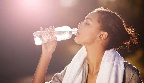 Drink meer water... Schot van een jonge vrouw drinken van een fles water na haar training. — Stockfoto