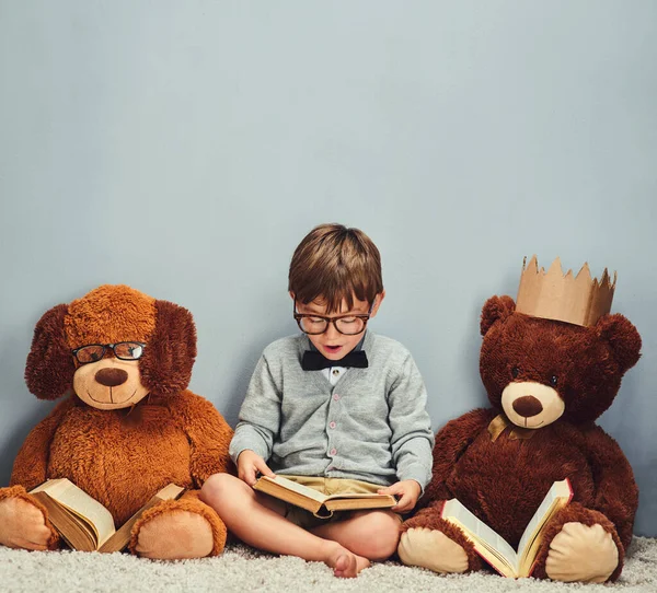 Ik ga wat lezen. Studio shot van een slimme jongen het lezen van een boek naast zijn teddyberen tegen een grijze achtergrond. — Stockfoto