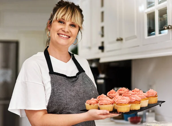 Paista itsesi onnelliseksi. Kasvatettu kuva naisesta, joka pitelee vastaleivottuja leivoksia keittiössään kotona. — kuvapankkivalokuva